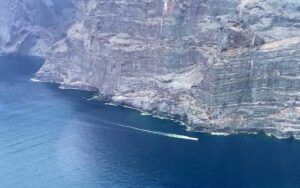 Experimente una impresionante vista aérea de los majestuosos Acantilados de Los Gigantes junto al océano azul profundo, con un barco dejando un rastro en el agua, durante nuestro "Tour en Helicóptero sobre los Acantilados de Los Gigantes y el Teide". - ForTwo - Planes para parejas