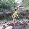 Con casco y arnés, una persona cruza un puente de cuerda sobre un arroyo, experimentando la emoción de la "Vía Ferrata en Huesca para Principiantes: Una Aventura Vertical entre Puentes y Escaleras" en los frondosos bosques de Huesca. - ForTwo - Planes para parejas