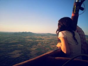 Una persona se inclina sobre la cesta de un globo aerostático, contemplando el impresionante paisaje de Mallorca y las montañas al atardecer durante un Vuelo en Globo en Mallorca desde Manacor. - ForTwo - Planes para parejas