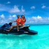 Dos personas con chalecos salvavidas disfrutan de deportes acuáticos en moto acuática, surcando las cristalinas aguas turquesas de Ibiza bajo un cielo parcialmente nublado. ¡Prueba "Deportes acuáticos en Ibiza y Formentera: Experiencia VIP" para una aventura exclusiva!. - ForTwo - Planes para parejas
