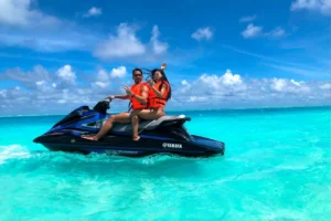 Dos personas con chalecos salvavidas disfrutan de deportes acuáticos en moto acuática, surcando las cristalinas aguas turquesas de Ibiza bajo un cielo parcialmente nublado. ¡Prueba "Deportes acuáticos en Ibiza y Formentera: Experiencia VIP" para una aventura exclusiva!. - ForTwo - Planes para parejas