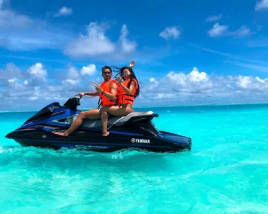 Dos personas con chalecos salvavidas disfrutan de deportes acuáticos en moto acuática, surcando las cristalinas aguas turquesas de Ibiza bajo un cielo parcialmente nublado. ¡Prueba "Deportes acuáticos en Ibiza y Formentera: Experiencia VIP" para una aventura exclusiva!. - ForTwo - Planes para parejas