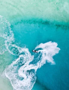 Vista aérea de una moto acuática creando estelas blancas y arremolinadas en las cristalinas aguas turquesas de Ibiza, mostrando la emoción de "Watersports en Ibiza y Formentera: Experiencia VIP. - ForTwo - Planes para parejas