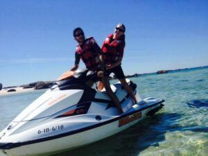 Dos personas disfrutando de "Alquila tu moto de agua en Vilagarcía de Arousa" en aguas claras y poco profundas cerca de una playa de arena, con chalecos salvavidas. - ForTwo - Planes para parejas