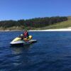 Alguien conduce una moto de agua amarilla por las cristalinas aguas azules cerca de la exuberante costa de Vilagarcía de Arousa bajo un cielo azul. ¡Alquila tu moto de agua en Vilagarcía de Arousa hoy!. - ForTwo - Planes para parejas