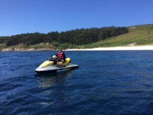 Alguien conduce una moto de agua amarilla por las cristalinas aguas azules cerca de la exuberante costa de Vilagarcía de Arousa bajo un cielo azul. ¡Alquila tu moto de agua en Vilagarcía de Arousa hoy!. - ForTwo - Planes para parejas