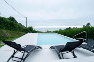 Dos tumbonas negras frente a una piscina al aire libre con vista al mar bajo un cielo nublado en el tranquilo Apartahotel en Playa de Valcovo, a solo unos pasos de la playa. - ForTwo - Planes para parejas