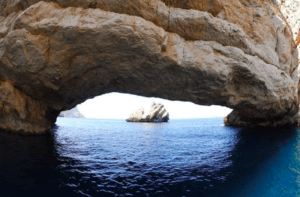 Experimente la impresionante belleza de un arco de piedra natural sobre tranquilas aguas azules, enmarcando una isla rocosa distante en su Aventura en lancha: Playas y cuevas de Ibiza, explorando impresionantes playas de Ibiza y joyas ocultas como cautivadoras cuevas. - ForTwo - Planes para parejas