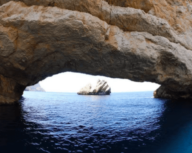 Experimente la impresionante belleza de un arco de piedra natural sobre tranquilas aguas azules, enmarcando una isla rocosa distante en su Aventura en lancha: Playas y cuevas de Ibiza, explorando impresionantes playas de Ibiza y joyas ocultas como cautivadoras cuevas. - ForTwo - Planes para parejas