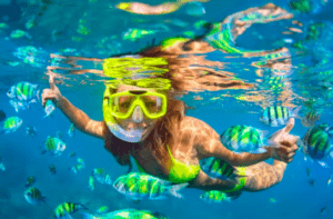 Una persona practicando snorkel entre vibrantes peces tropicales con un tubo y una máscara amarillos en las cristalinas aguas azules cerca de las pintorescas playas de Ibiza, como parte de la experiencia Aventura en lancha: Playas y cuevas de Ibiza. - ForTwo - Planes para parejas
