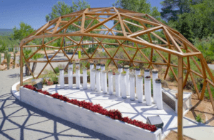 En BIBO PARK Ibiza: Naturaleza y biotecnología, una elegante cúpula de madera abierta con columnas cilíndricas blancas se alza entre vibrantes flores rojas bajo el cielo azul claro. - ForTwo - Planes para parejas