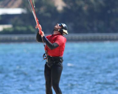 En una playa de arena de Pontevedra, alguien con una camiseta roja disfruta de su primera clase de kitesurf, bautismo de kitesurf en Pontevedra, mientras maniobra una cometa con el inmenso océano como telón de fondo. - ForTwo - Planes para parejas