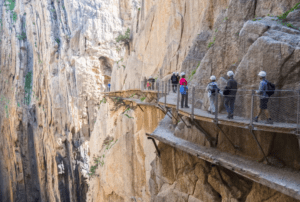 Con cascos, la gente recorre los estrechos senderos del "Caminito del Rey: Aventura desde Málaga", un viaje icónico a través de impresionantes formaciones rocosas en un acantilado de Málaga. - ForTwo - Planes para parejas