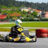 Con casco puesto, un corredor acelera en un kart en el Kartódromo Valga con montones de neumáticos y casas con encanto cerca, capturando la emoción de "Carreras de karts en Kartódromo Valga en Pontevedra. - ForTwo - Planes para parejas