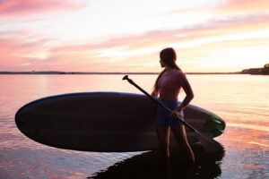 Al atardecer, en las brillantes aguas de O Grove, una persona maniobra hábilmente su tabla de paddle surf como si asistiera a una sesión improvisada de "Clases de Paddle Surf en O Grove" bajo un cielo pintado de tonos brillantes. - ForTwo - Planes para parejas