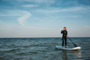 Vestido con un traje de neopreno, alguien saborea el paddleboarding en el mar tranquilo bajo un cielo azul claro, capturando la esencia de las Clases de Paddle Surf en O Grove. - ForTwo - Planes para parejas