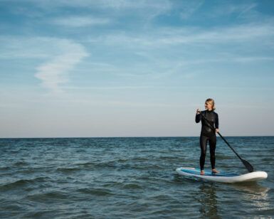 Vestido con un traje de neopreno, alguien saborea el paddleboarding en el mar tranquilo bajo un cielo azul claro, capturando la esencia de las Clases de Paddle Surf en O Grove. - ForTwo - Planes para parejas
