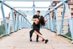 Una pareja baila apasionadamente en un puente peatonal al aire libre en Vigo, integrándose maravillosamente con el entorno urbano, inspirado en "Clases de Salsa y Bachata en Vigo". - ForTwo - Planes para parejas