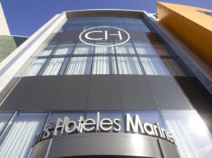 La moderna fachada con grandes ventanales y un destacado logotipo CH da la bienvenida a los huéspedes a HTLS Hoteles Marines, ofreciendo una escapada ideal para una escapada romántica que recuerda a la famosa Escapada romántica en el Hotel Carris Marineda. - ForTwo - Planes para parejas