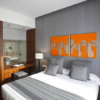 Experimente la elegancia moderna en el Hotel Carris Marineda con una lujosa cama doble, acogedoras almohadas grises y vibrantes obras de arte en naranja. Ideal para una escapada romántica en el Hotel Carris Marineda, disfrute de la vista única del baño, que combina diseño contemporáneo con un encanto romántico. - ForTwo - Planes para parejas