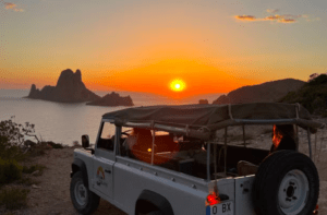 Un SUV Excursión 4x4 está estacionado en un acantilado al atardecer, con vistas al océano y las formaciones rocosas durante la "Excursión 4x4, senderismo y barco en Ibiza. - ForTwo - Planes para parejas