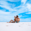 Una pareja se relaja en una playa soleada de Formentera, experimentando su pedazo personal de paraíso bajo un cielo azul vibrante con nubes blancas, como se describe en "Excursión a Formentera: Un día en el paraíso". - ForTwo - Planes para parejas