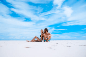 Una pareja se relaja en una playa soleada de Formentera, experimentando su pedazo personal de paraíso bajo un cielo azul vibrante con nubes blancas, como se describe en "Excursión a Formentera: Un día en el paraíso". - ForTwo - Planes para parejas