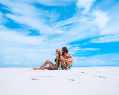 Una pareja se relaja en una playa soleada de Formentera, experimentando su pedazo personal de paraíso bajo un cielo azul vibrante con nubes blancas, como se describe en "Excursión a Formentera: Un día en el paraíso". - ForTwo - Planes para parejas