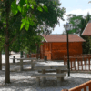 Cabañas de madera y mesas de picnic descansan bajo árboles soleados en un tranquilo parque con senderos de grava que serpentean junto a una farola. Ideal para una escapada de fin de semana en el Embalse de Negratín, rodeado de una serena belleza. - ForTwo - Planes para parejas