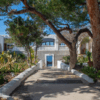 Un camino arbolado conduce al Hostal La Torre Ibiza Cap Negre Ibiza, un edificio blanco adornado con arcos, que ofrece impresionantes vistas al mar que recuerdan el encanto de Ibiza. - ForTwo - Planes para parejas
