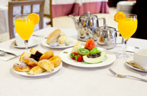 La mesa de desayuno del Hotel Badajoz Center, con un mantel blanco impecable, derrocha modernidad y bienestar, ofreciendo bollería, fruta fresca, zumo de naranja y té como un lujoso ritual matutino. - ForTwo - Planes para parejas