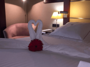 En el acogedor Hotel Badajoz Center, las toallas dobladas en cisnes forman un corazón sobre una cama con una flor roja, fusionando a la perfección modernidad y bienestar. - ForTwo - Planes para parejas