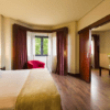 Disfrute de la modernidad y el bienestar en el Hotel Badajoz Center en una espaciosa habitación con una cama King, suelo de madera y puertas corredizas que conducen a una zona de estar con una silla roja. - ForTwo - Planes para parejas