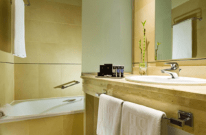 El moderno baño del Hotel Badajoz Center cuenta con un elegante lavabo, espejo y bañera. Las toallas están convenientemente colgadas cerca y los artículos de aseo están cuidadosamente dispuestos en la encimera para mayor bienestar. - ForTwo - Planes para parejas