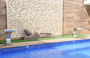 La serena zona de piscina del Hotel Florencio Ibiza en San Antoni cuenta con una pared de piedra con motivos florales y una estatua reclinada, complementada por dos fuentes de agua metálicas para darle un toque elegante. - ForTwo - Planes para parejas