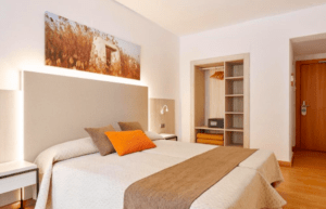 Experimente el acogedor encanto del Hotel Florencio Ibiza en San Antoni. Esta habitación cuenta con una cama doble, tonos neutros, un armario abierto, obras de arte paisajísticas e iluminación cálida, perfecta para sumergirse en la vibrante energía de San Antoni. - ForTwo - Planes para parejas