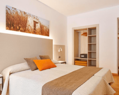 Experimente el acogedor encanto del Hotel Florencio Ibiza en San Antoni. Esta habitación cuenta con una cama doble, tonos neutros, un armario abierto, obras de arte paisajísticas e iluminación cálida, perfecta para sumergirse en la vibrante energía de San Antoni. - ForTwo - Planes para parejas
