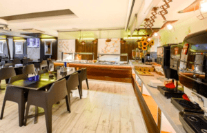 La elegante estación de buffet, las sillas negras, los girasoles vibrantes, las máquinas de café y la iluminación cálida crean un interior de restaurante moderno y acogedor en el Hotel Florencio Ibiza en San Antoni. - ForTwo - Planes para parejas