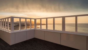La terraza de la azotea del Hotel Riazor en La Coruña ofrece una impresionante vista del atardecer, con el océano y el horizonte de La Coruña en la distancia contra un cielo cálido. - ForTwo - Planes para parejas