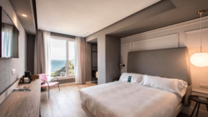 Alójese en el Hotel Riazor en La Coruña y disfrute de una moderna habitación con una cama grande, escritorio y TV. Cortinas transparentes enmarcan impresionantes vistas al mar para una experiencia encantadora desde su ventana. - ForTwo - Planes para parejas