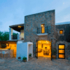 Un edificio rústico de piedra con un interior iluminado, asientos al aire libre y árboles bajo un cielo oscuro, perfecto para una escapada idílica en el Hotel Rural: Escapada al corazón de Ibiza. - ForTwo - Planes para parejas