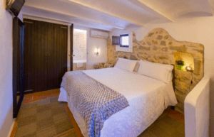 Disfrute de una acogedora habitación en el Hotel Rural: Escapada al corazón de Ibiza, con cama doble, paredes con detalles de piedra y armario de madera. Este idílico entorno incluye una encantadora ventana pequeña, el refugio perfecto. - ForTwo - Planes para parejas