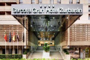 La entrada del Hotel en el Corazón Badajoz presenta una elegante escalera, una elegante marquesina de cristal y cuatro mástiles de bandera a la izquierda. - ForTwo - Planes para parejas