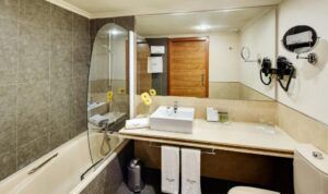 Experimente el encanto del Hotel en el Corazón Badajoz en este moderno baño con bañera, lavabo, espejo grande, secador de pelo y lujosas toallas. Las flores frescas en el mostrador le dan un toque de elegancia a su estancia. - ForTwo - Planes para parejas