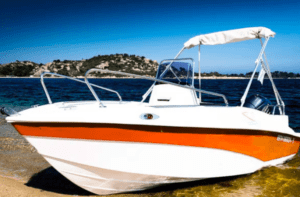 Una lancha motora blanca y naranja descansa sobre una playa de arena con agua azul y colinas distantes bajo un cielo despejado, invitándote a explorar con "Navega Ibiza a tu Ritmo: Barcos sin Licencia". - ForTwo - Planes para parejas
