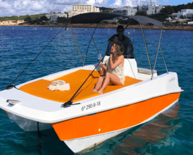 Dos personas se relajan en un barco naranja y blanco en las aguas cristalinas de una orilla de arena, abrazando el espíritu de "Navega Ibiza a tu Ritmo: Barcos sin Licencia" mientras exploran sin límites. - ForTwo - Planes para parejas