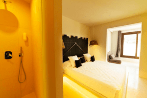 Una acogedora habitación en PAIISE Hotels Ibiza ofrece una cama grande, una ducha adyacente y una relajante vista desde la ventana. - ForTwo - Planes para parejas