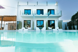 Esta moderna villa blanca, con amplios ventanales y balcones, ofrece vistas a una piscina cristalina y un remanso de paz. Combinando lujo y relajación bajo un cielo azul despejado, evoca la esencia de PAIISE Hotels Ibiza: Relájate cerca de las playas. - ForTwo - Planes para parejas
