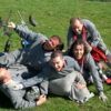 Un grupo de hombres con uniformes iguales, riendo y jugando, amontonados unos sobre otros en el césped de Asturias, con sus marcadores de Paintball en Asturias: ¡Juegos de guerra en el bosque! esparcidos cerca, listos para más acción. - ForTwo - Planes para parejas
