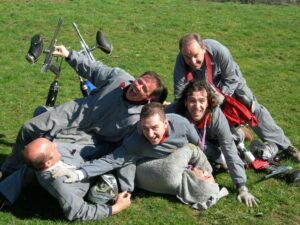 Un grupo de hombres con uniformes iguales, riendo y jugando, amontonados unos sobre otros en el césped de Asturias, con sus marcadores de Paintball en Asturias: ¡Juegos de guerra en el bosque! esparcidos cerca, listos para más acción. - ForTwo - Planes para parejas